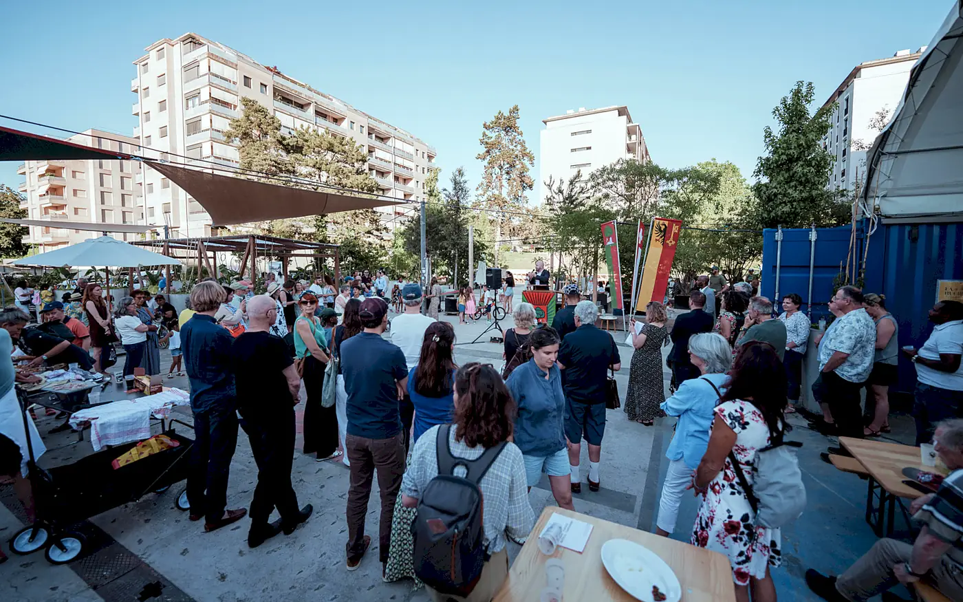 La place de la Tambourine noire de monde le soir de l’inauguration des aménagements du quartier, bannières de Carouge, de Genève et de la Suisse