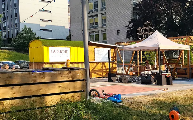 La buvette jaune La Ruche au toit végétalisé, avec sa scène en bois, juin 2023